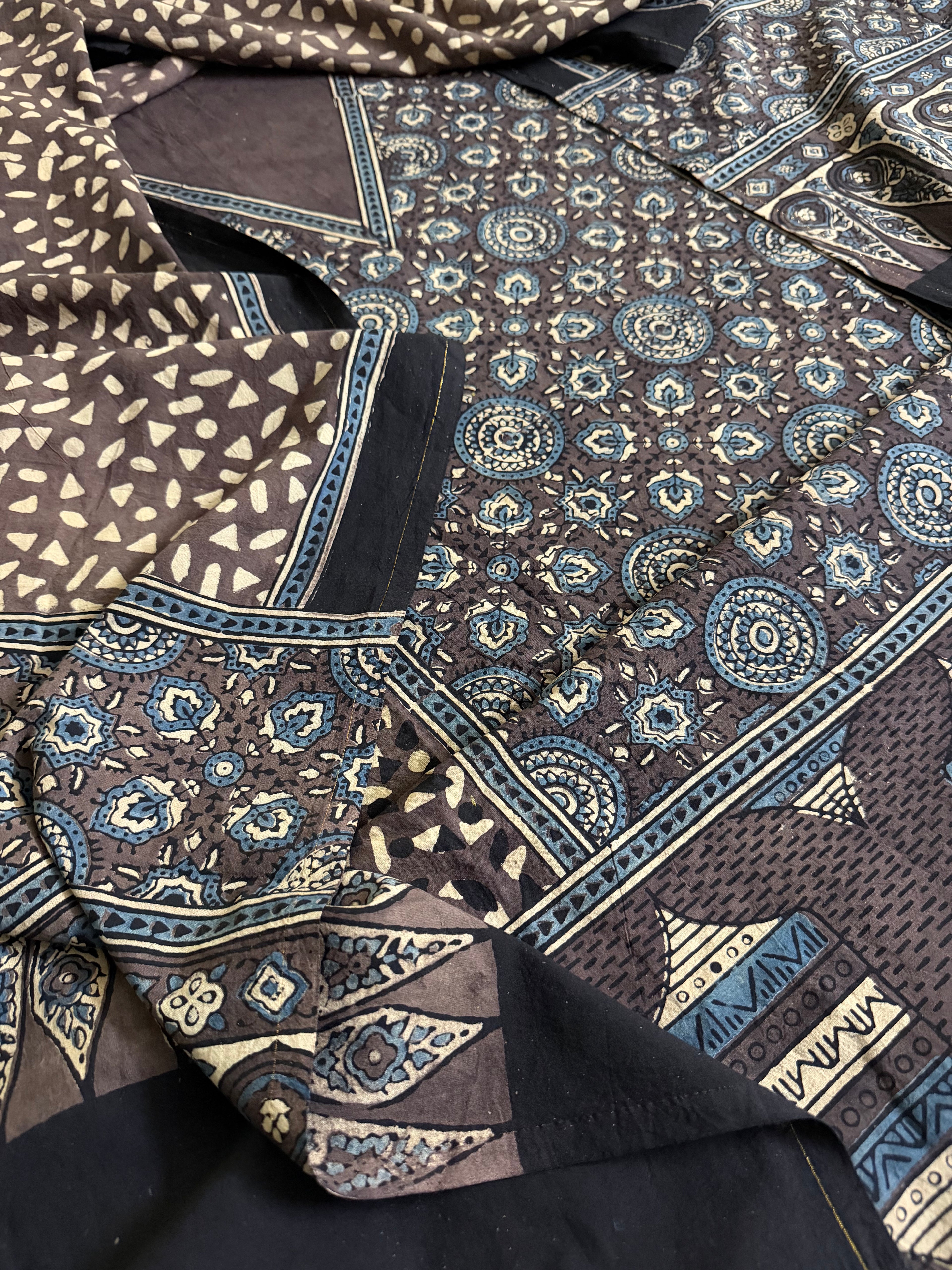 Flat lay of brown Ajrakh cotton unstitched suit set showing kurta, salwar, and dupatta with traditional hand block print in earthy brown and indigo blue