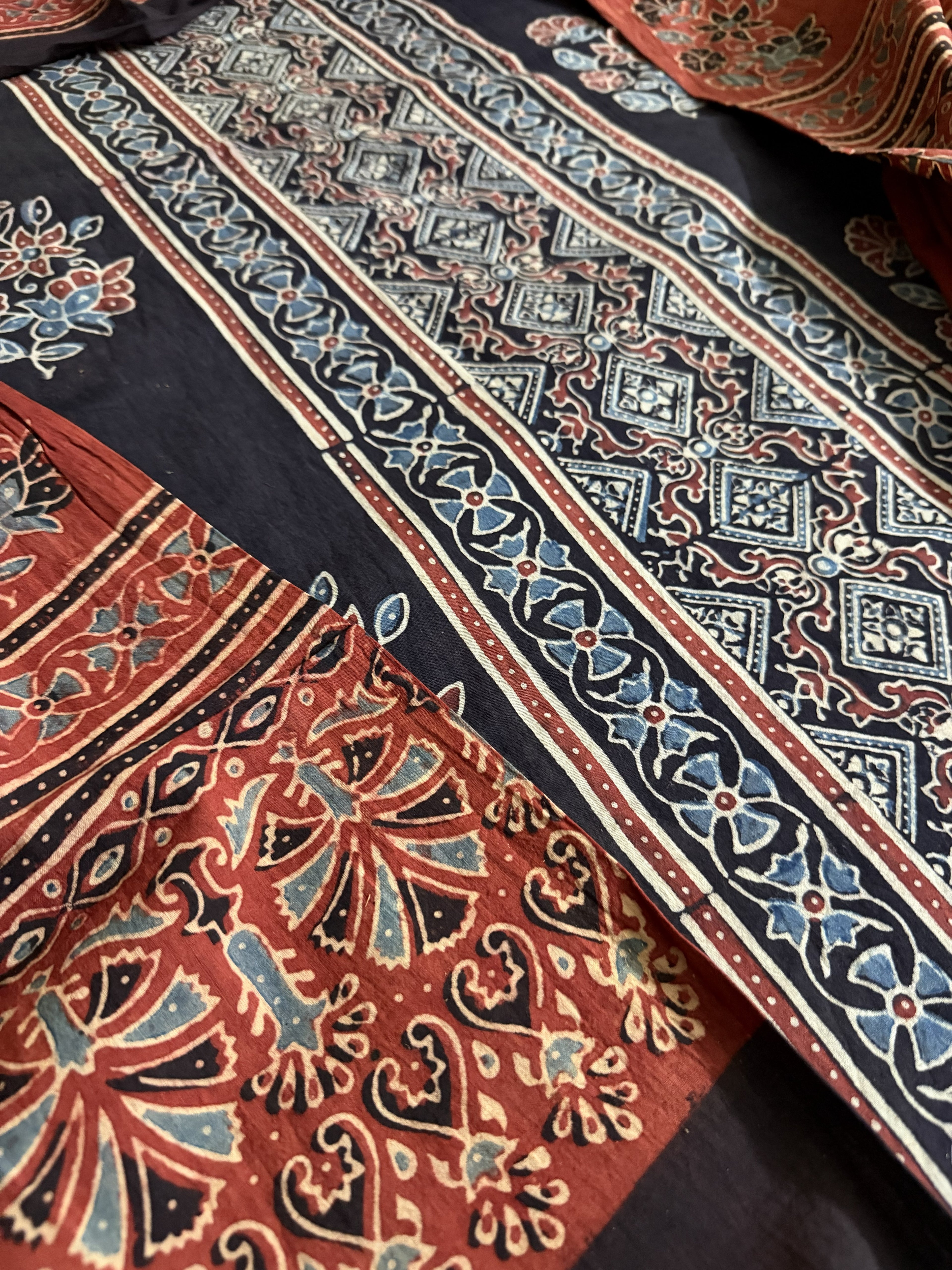 Close-up of black Ajrakh cotton kurta fabric with diamond geometric block print border and red dupatta featuring large paisley and floral hand block print in indigo and rust tones