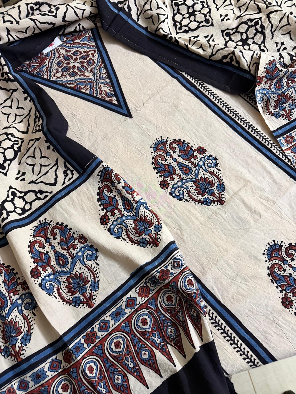 Close-up of oatmeal Ajrakh cotton kurta with large blue and red paisley medallion block print, intricate navy border with scrolling floral and geometric motifs, and black Ajrakh dupatta with lattice print
