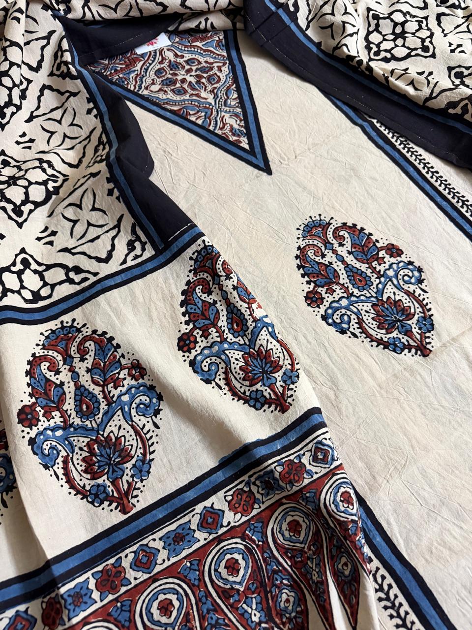 Close-up of oatmeal cotton kurta with blue and red paisley medallion Ajrakh block print, navy blue border stripe, and black geometric Ajrakh dupatta with floral lattice pattern