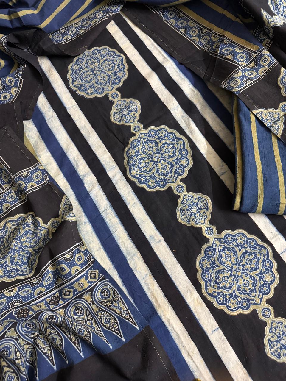 Close-up of black Ajrakh cotton kurta fabric with white stripe pattern, large blue and gold medallion block print motifs, and blue Ajrakh dupatta with geometric border