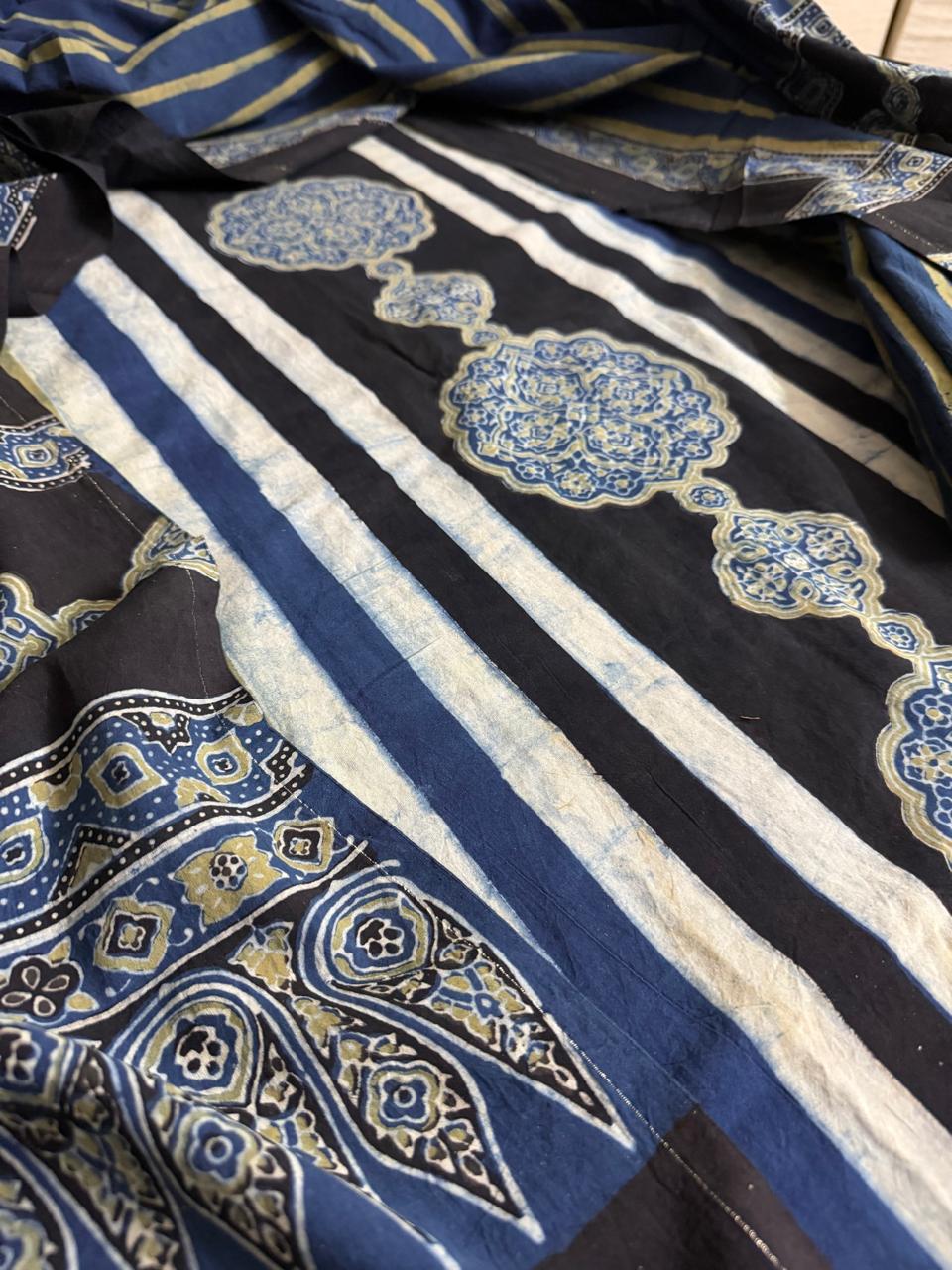 Close-up flat lay of black Ajrakh cotton kurta with white stripe and blue gold medallion hand block print, alongside blue Ajrakh dupatta with paisley and geometric border print"