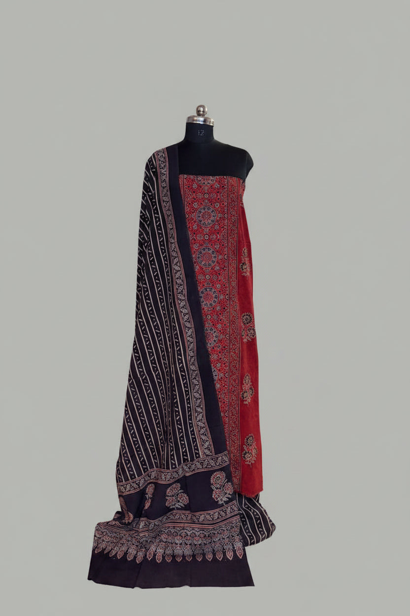 Red and black Ajrakh cotton 3-piece unstitched suit set on mannequin — deep red kurta with intricate medallion block print, black striped dupatta with floral Ajrakh border and tassel hem