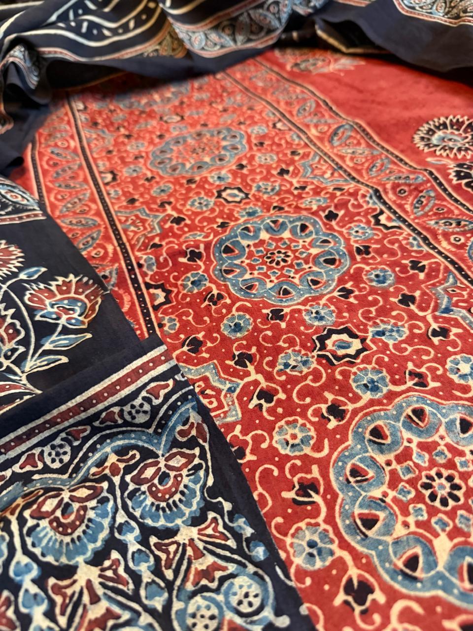 Close-up of red Ajrakh cotton kurta with circular medallion and scrolling floral hand block print alongside black Ajrakh dupatta border with blue and red paisley motifs