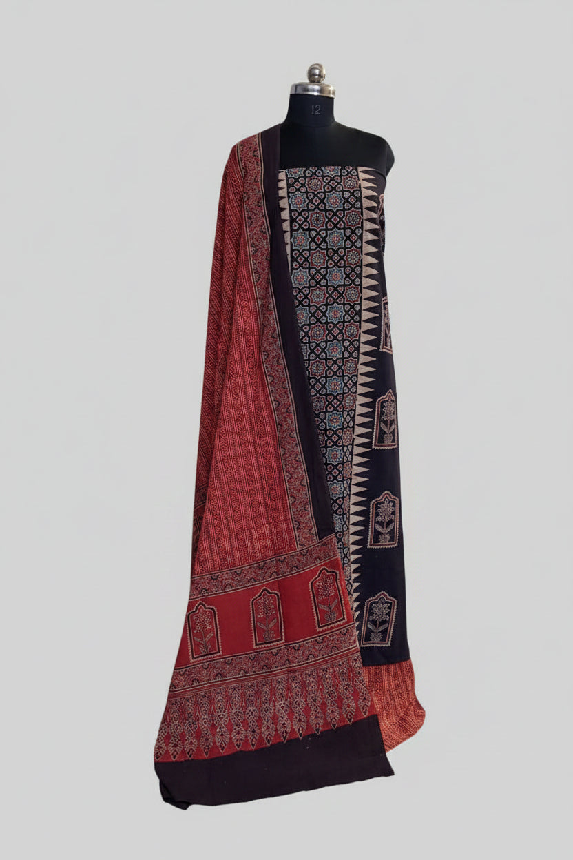 Black and red Ajrakh cotton 3-piece unstitched suit set on mannequin — deep black kurta with geometric star lattice and zigzag border block print, floral arch panels, and red Ajrakh dupatta with dense floral print