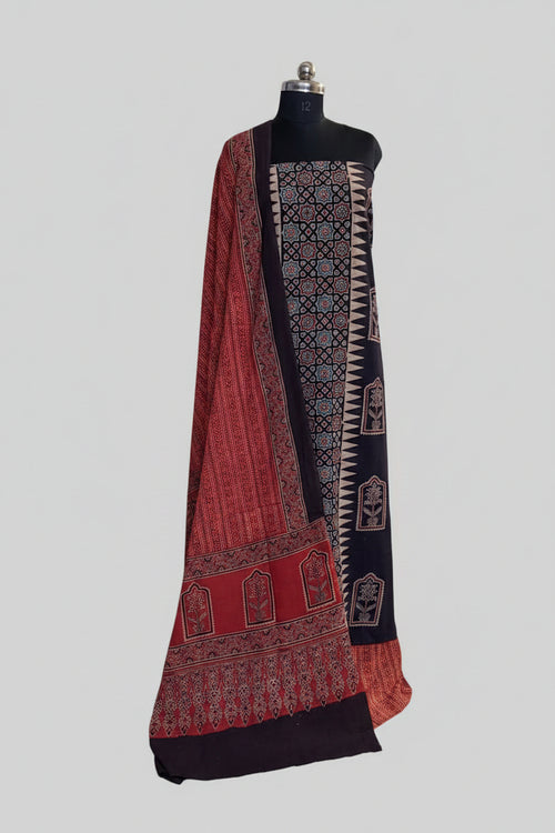 Black and red Ajrakh cotton 3-piece unstitched suit set on mannequin — deep black kurta with geometric star lattice and zigzag border block print, floral arch panels, and red Ajrakh dupatta with dense floral print