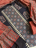 Flat lay of black Ajrakh cotton kurta fabric with geometric star lattice and cream zigzag border block print, floral arch motif panels, alongside red Ajrakh dupatta with dense floral and paisley print
