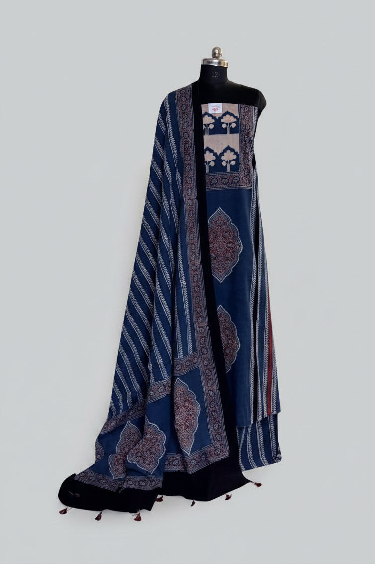 Blue and black Ajrakh cotton 3-piece unstitched suit set on mannequin — indigo blue kurta with cream tree-of-life panel and red medallion block print, blue dupatta with diagonal stripe and tassel hem
