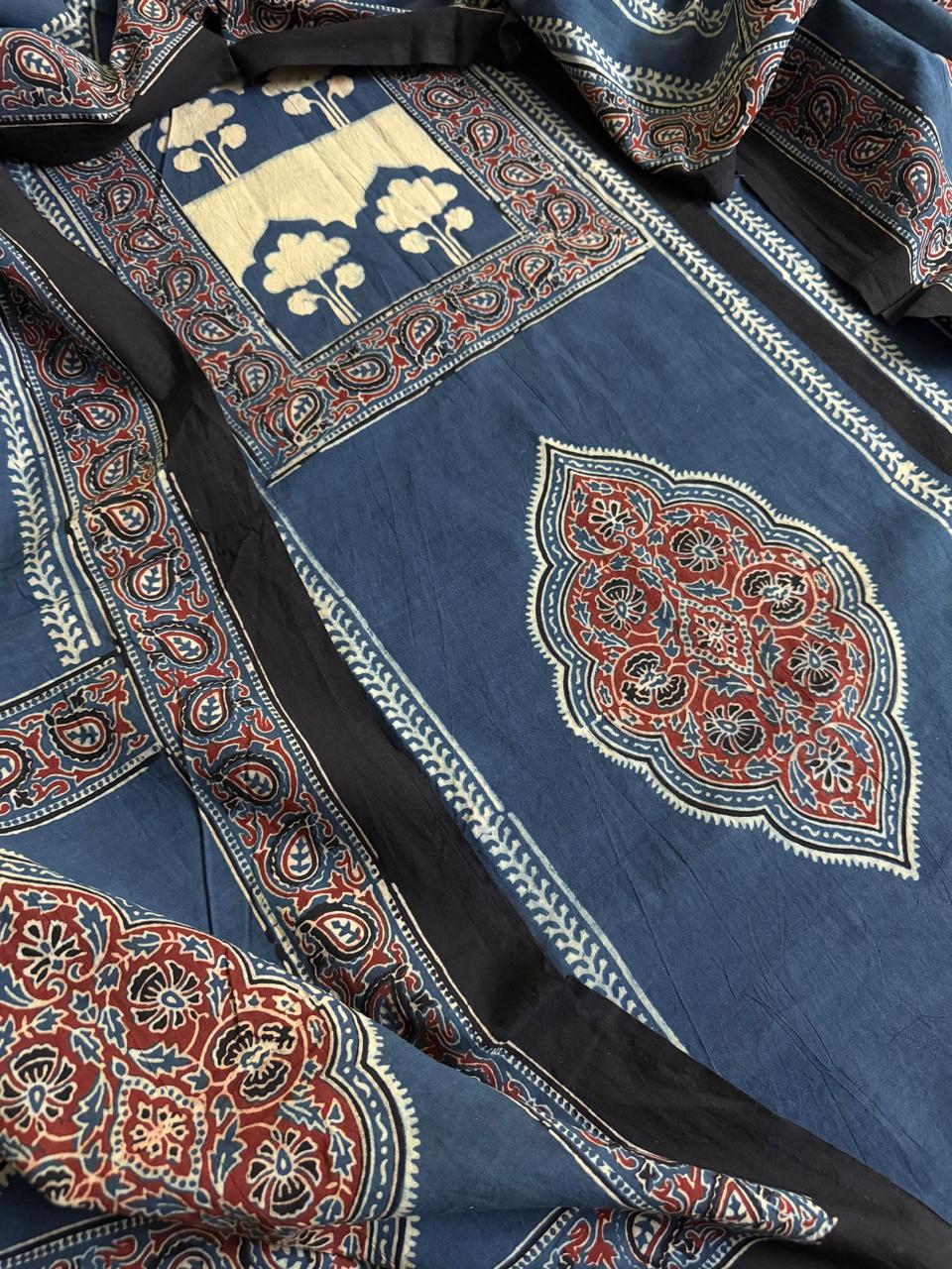 Close-up flat lay of indigo blue Ajrakh cotton kurta with cream tree-of-life block print panel, red floral medallion motif, and blue dupatta with dense red paisley border print