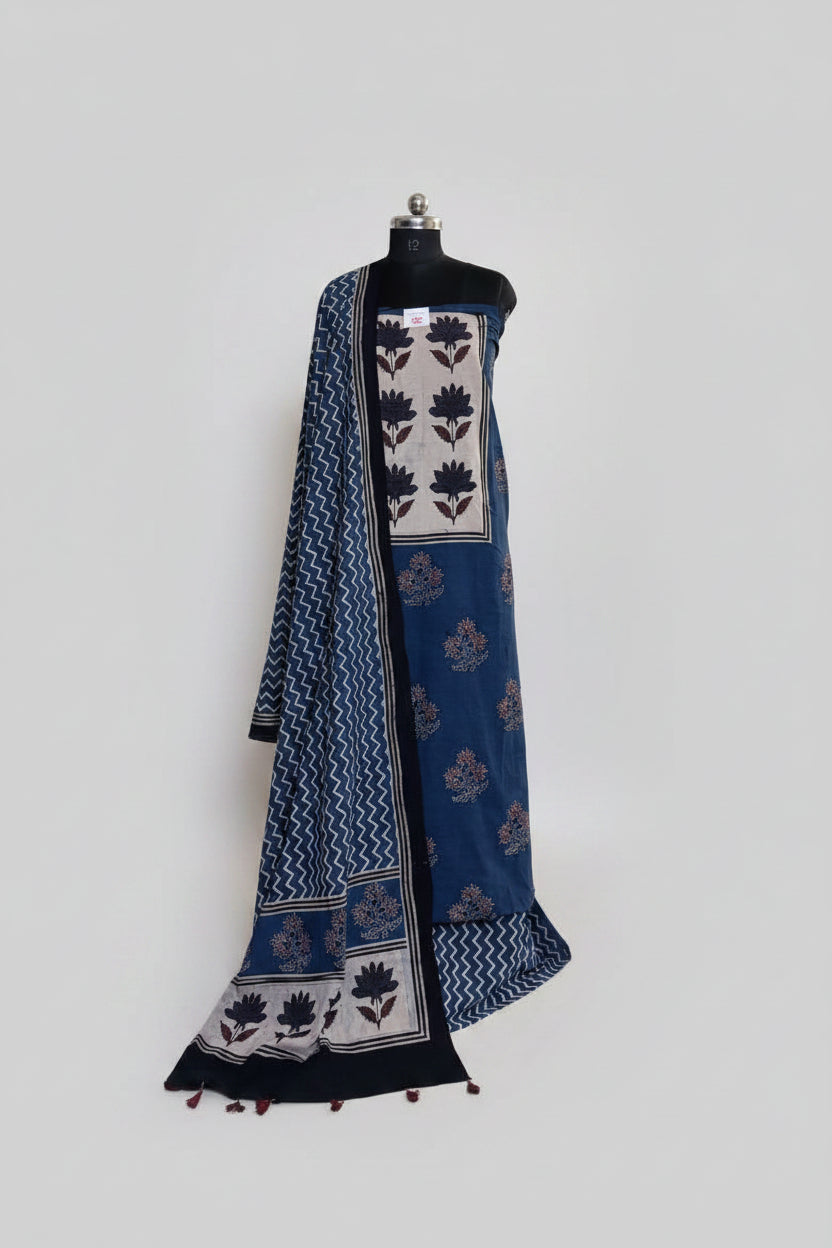 Blue and black Ajrakh floral block print cotton 3-piece unstitched suit set on mannequin — indigo blue kurta with cream floral yoke panel, scattered floral body print, and blue zigzag chevron dupatta with tassel hem