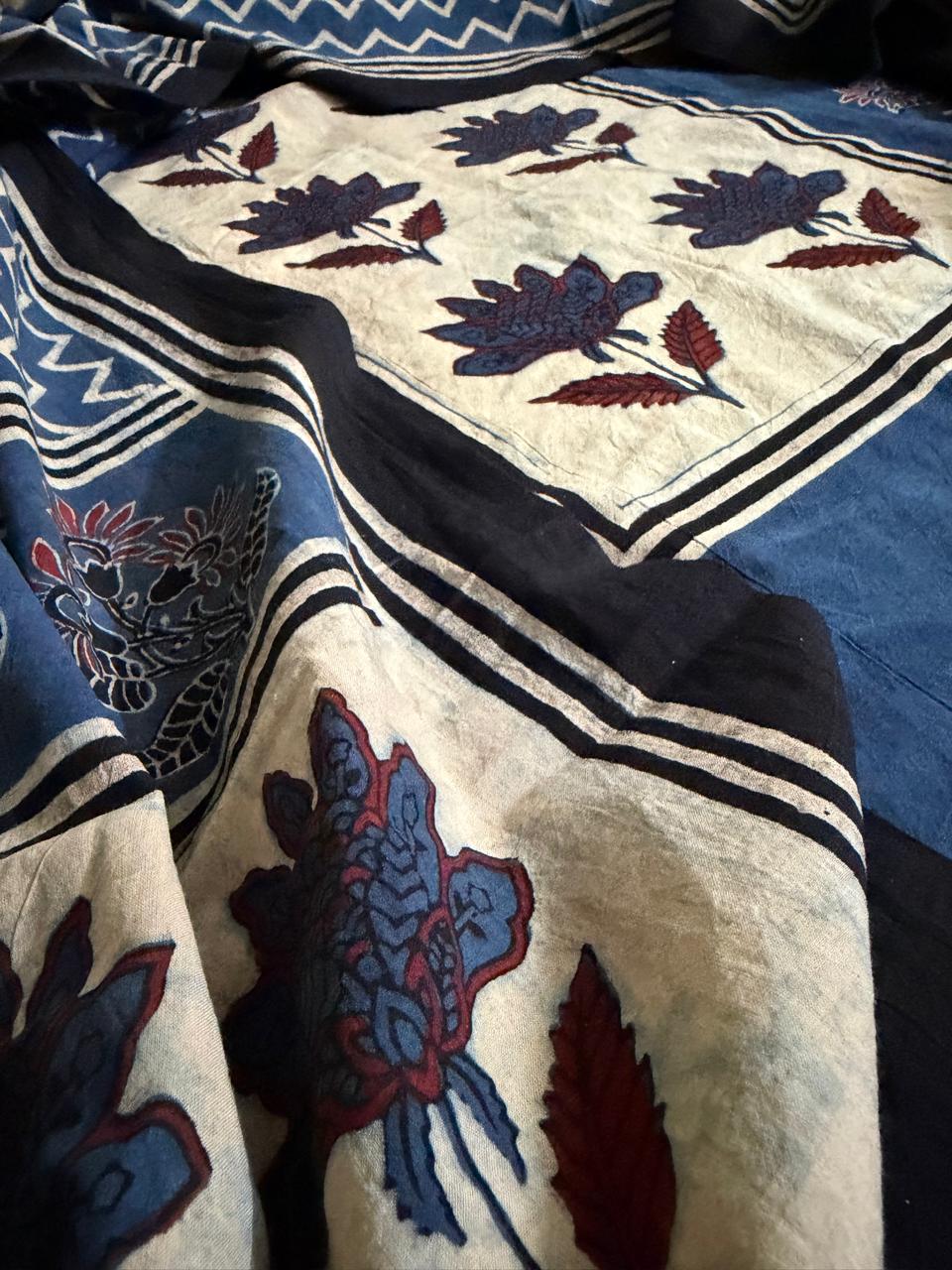 Close-up of cream Ajrakh cotton kurta hem with large blue and red floral bouquet block print, black border stripe, and indigo blue zigzag chevron dupatta in background