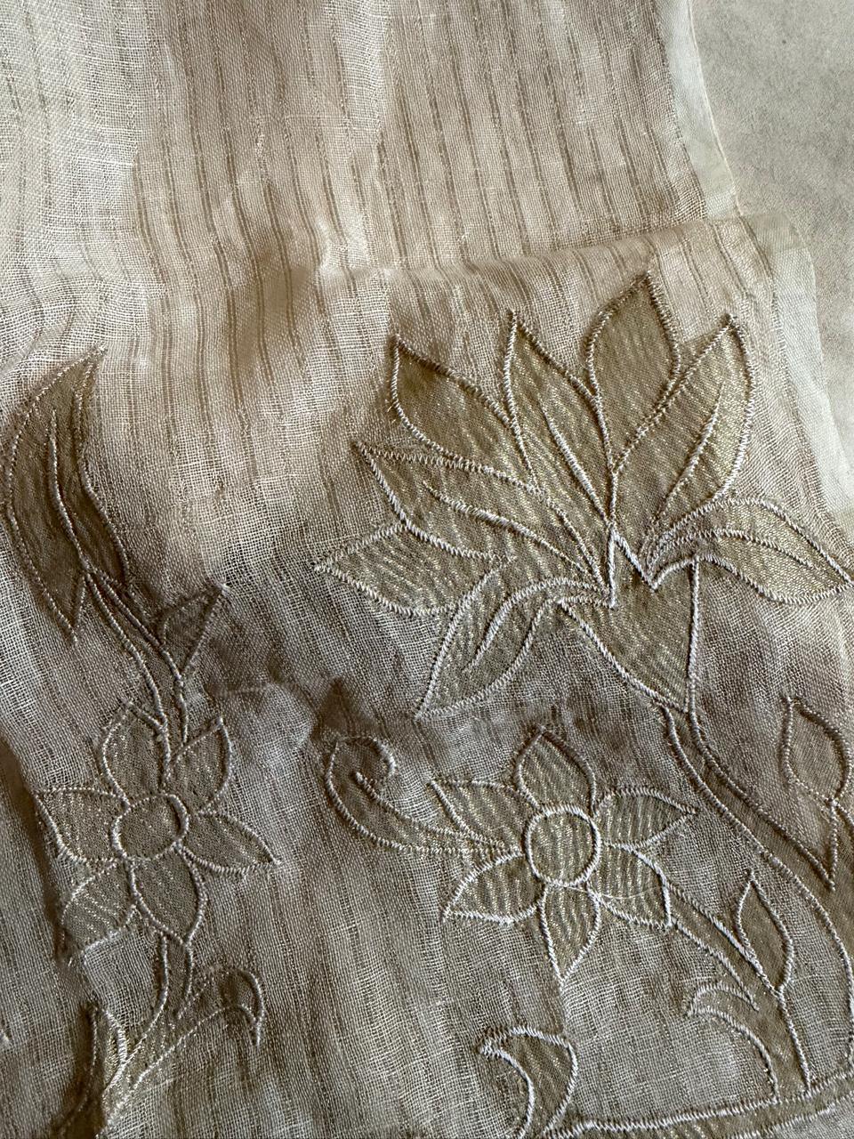 Close-up of beige linen fabric showing intricate gold applique lotus and floral motif border embroidery