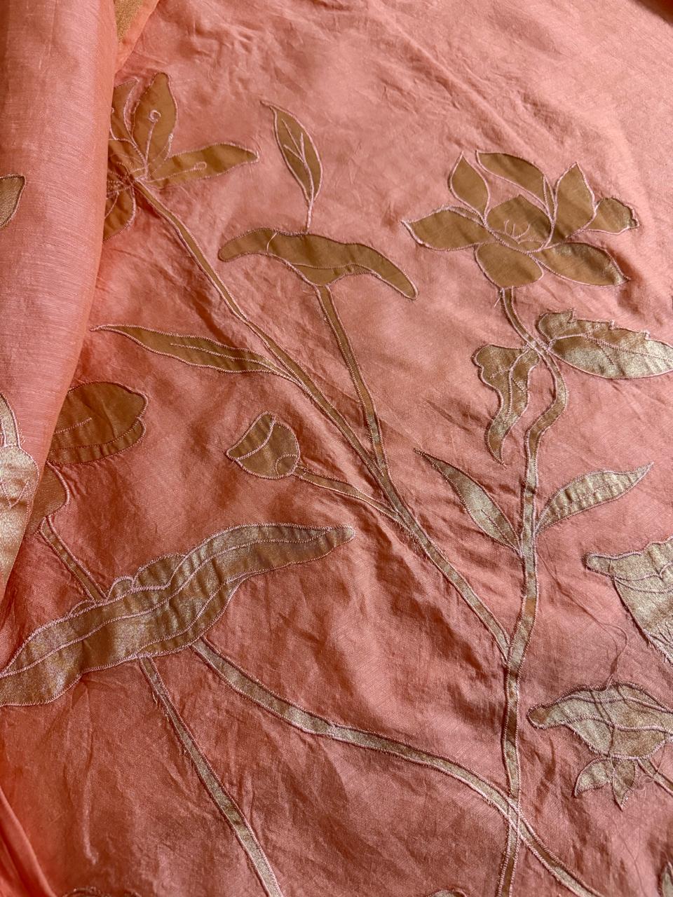 Close-up of peach beige Chanderi silk kurta fabric with gold appliqué tall stem, lotus flower and leaf botanical motifs