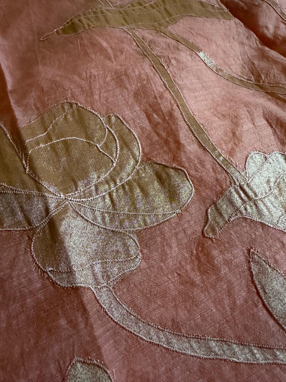 Macro close-up of peach beige Chanderi silk fabric with large gold silk tissue appliqué rose bloom and dragonfly motif detail