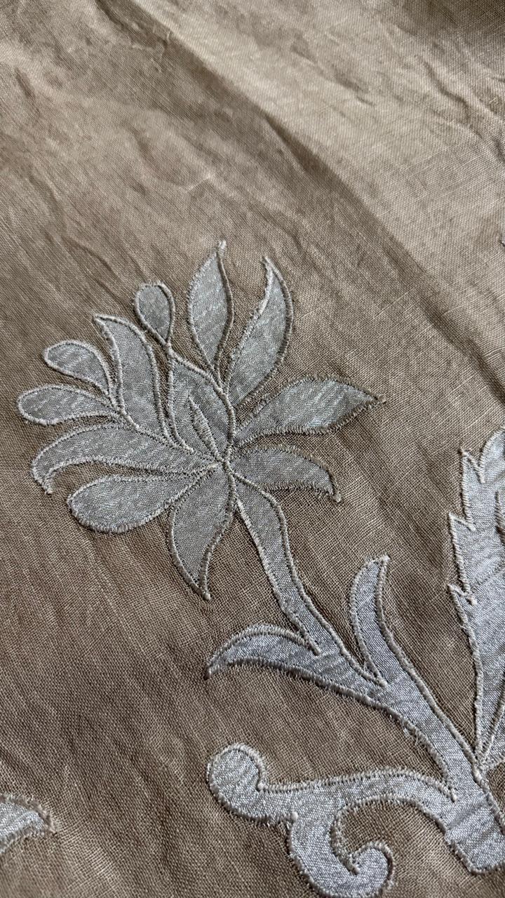 Macro close-up of silver silk tissue appliqué lotus flower motif on taupe linen fabric