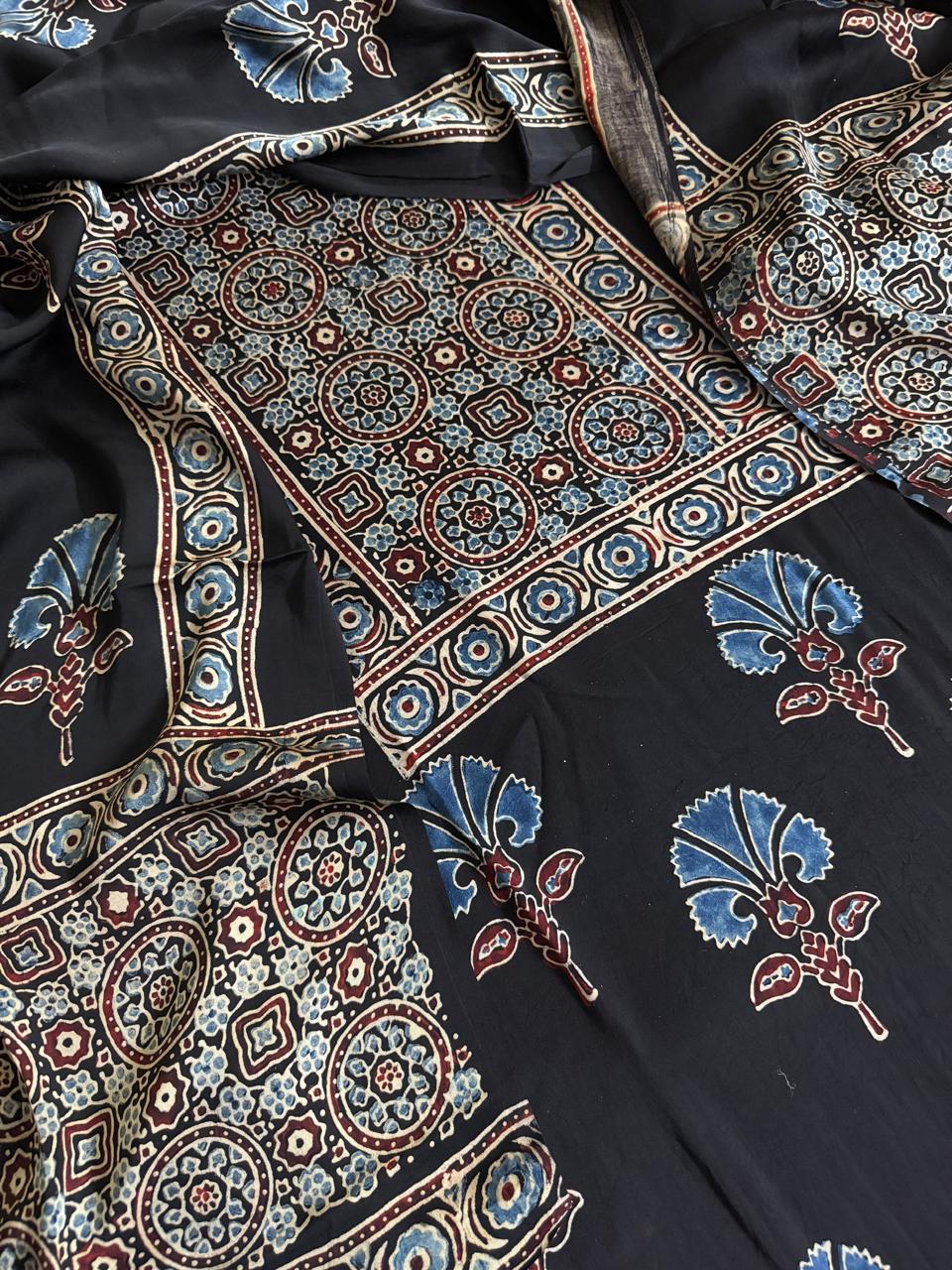 Flat lay of black Ajrakh Modal silk kurta dupatta set showing blue and maroon geometric medallion yoke panel, scattered blue glory lily floral body print and dupatta