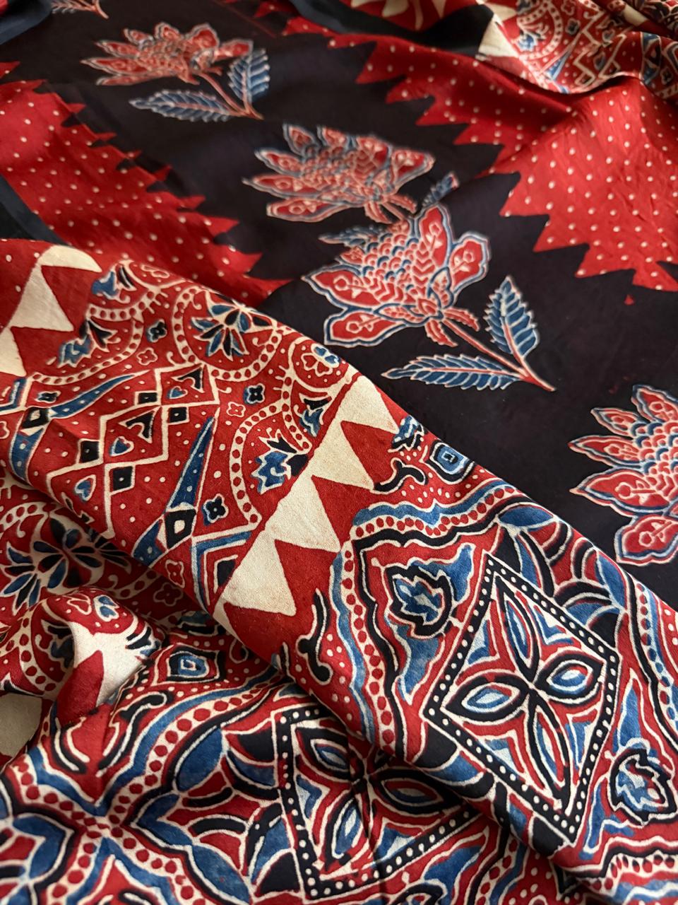Macro close-up of red Ajrakh Modal silk dupatta with red, blue and black geometric diamond and paisley block print, alongside black zigzag floral kurta border