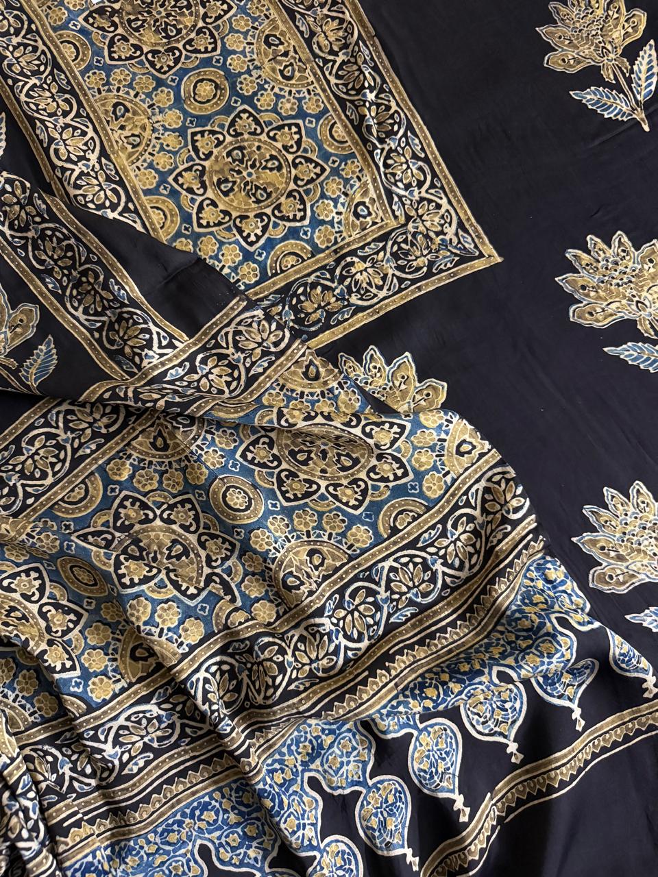 Close-up of black modal silk Ajrakh fabric pieces showing blue and gold geometric medallion yoke, lotus body print and dense paisley dupatta border