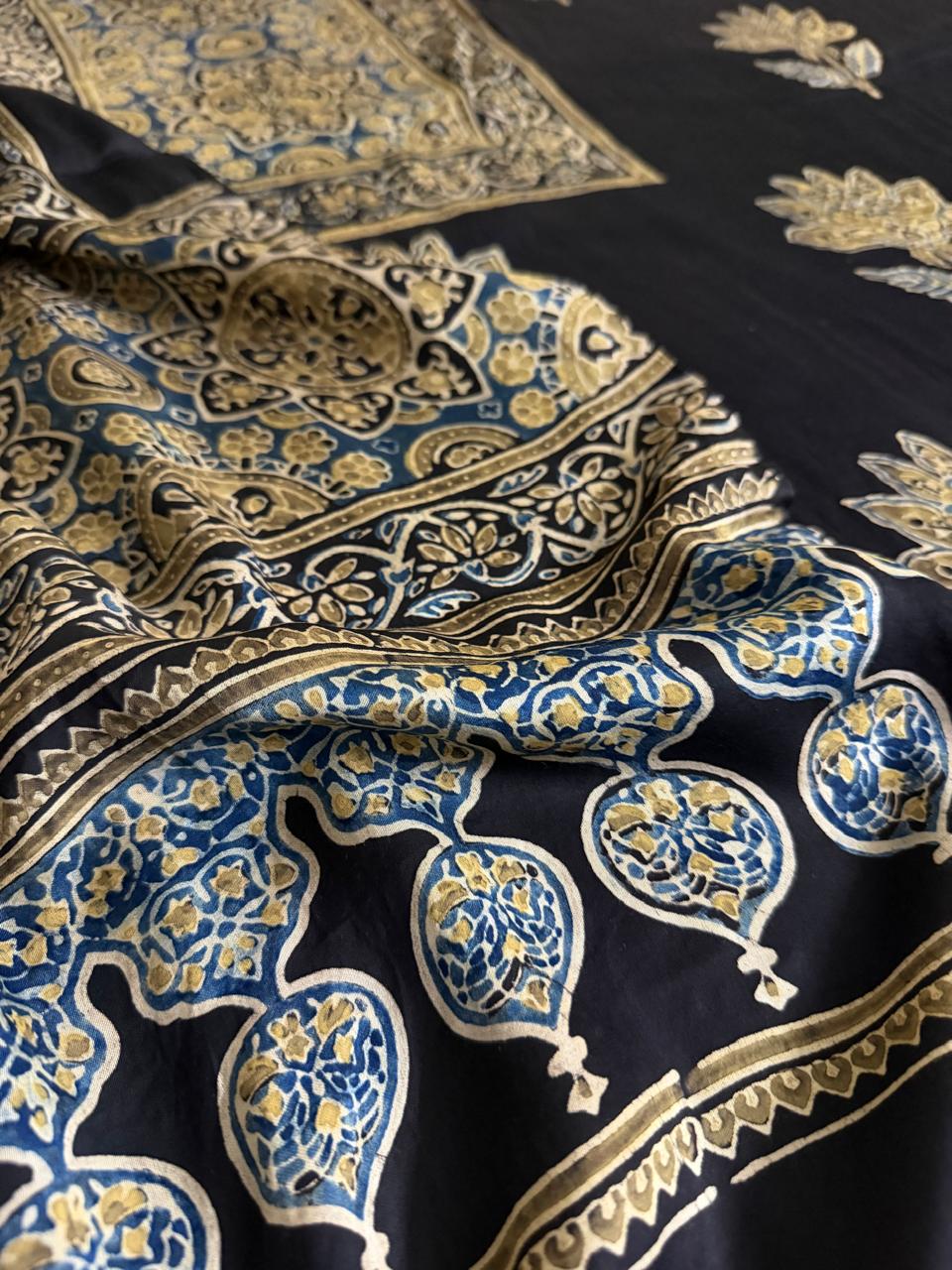 Macro close-up of black modal silk Ajrakh dupatta with large blue and gold paisley, floral and medallion block print border in rich detail