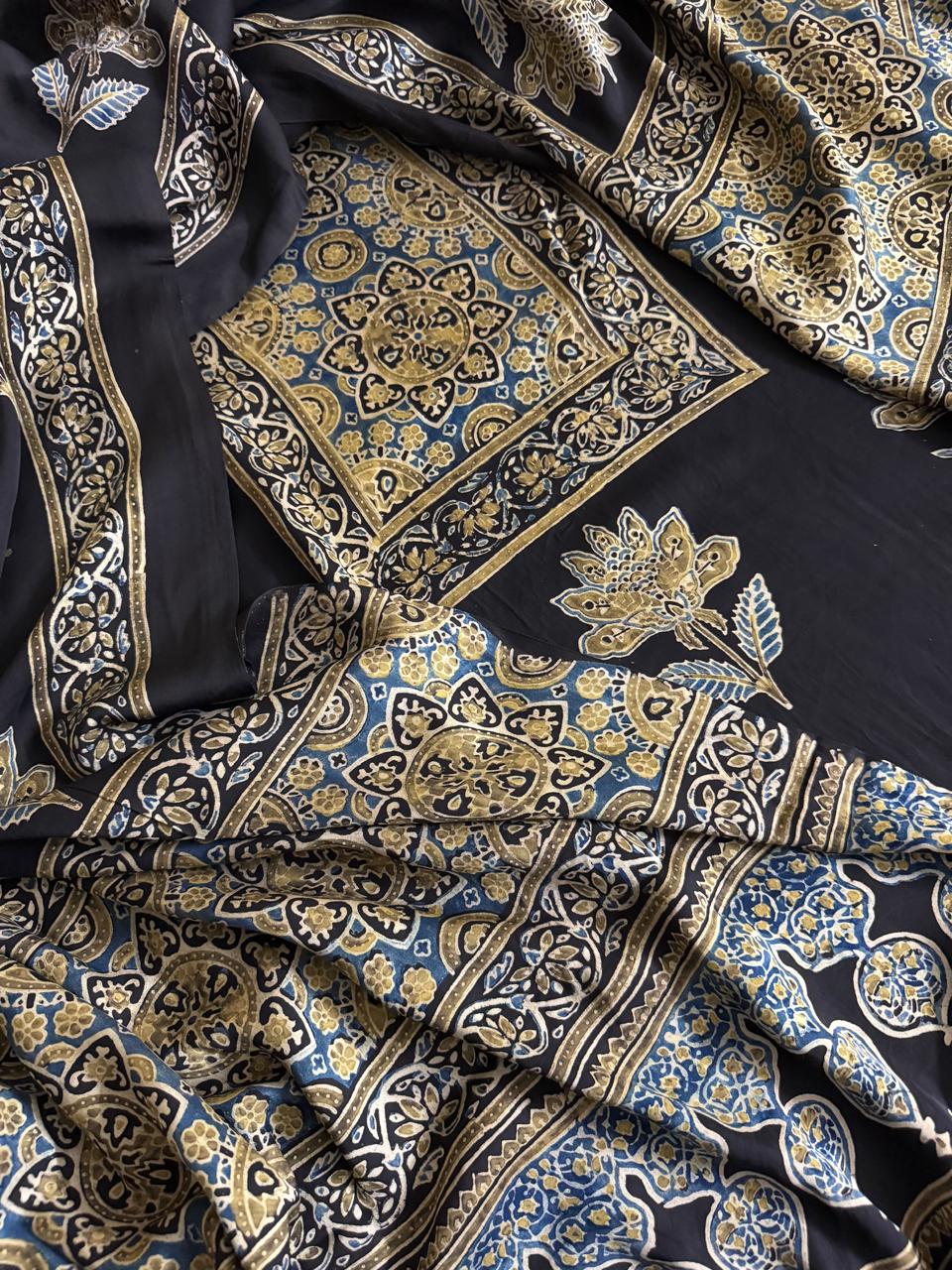 Flat lay of black modal silk Ajrakh kurta dupatta set showing blue and gold medallion yoke panel, scattered lotus body print and intricate paisley dupatta border