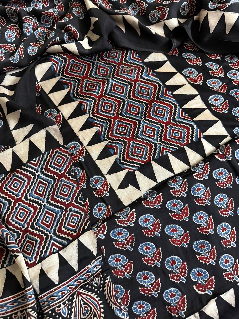 Flat lay of black modal silk Ajrakh kurta dupatta set showing red and blue geometric diamond yoke, floral body print and triangle border pieces