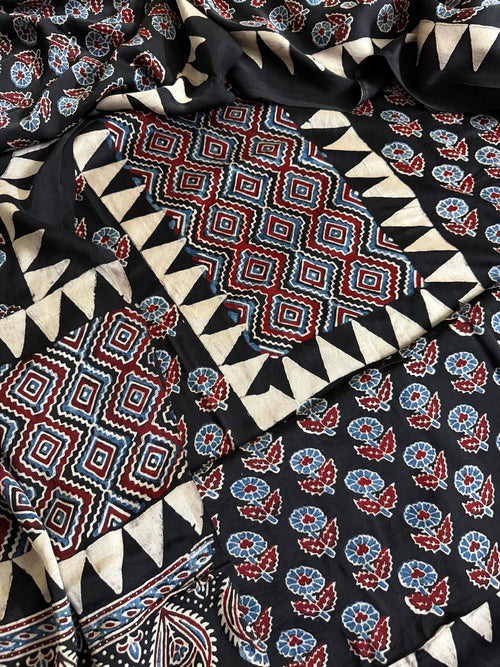 Flat lay of black modal silk Ajrakh kurta dupatta set showing red and blue geometric diamond yoke, floral body print and triangle border pieces