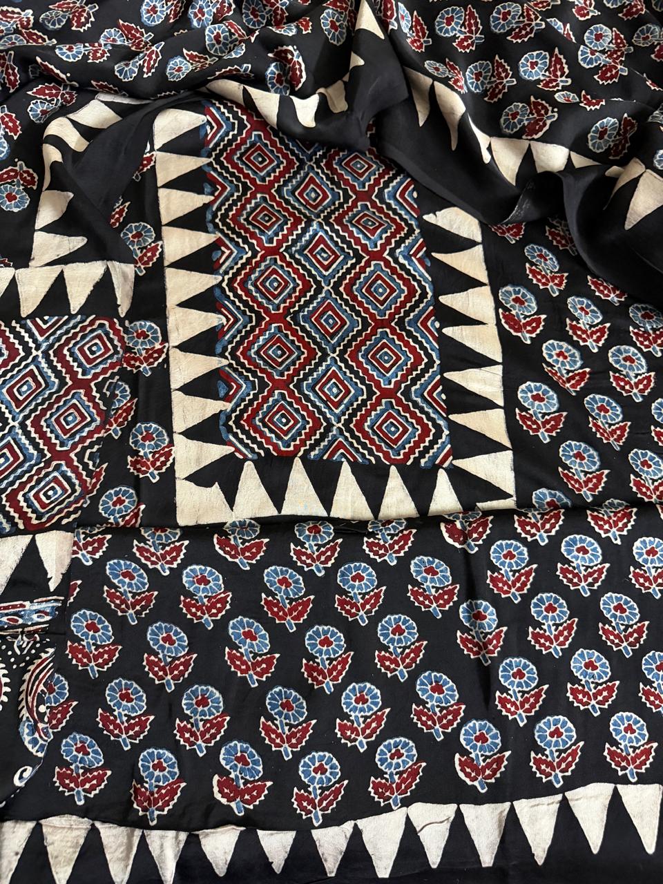 Close-up of black modal silk Ajrakh kurta fabric with red and blue geometric diamond yoke panel and scattered floral block print body