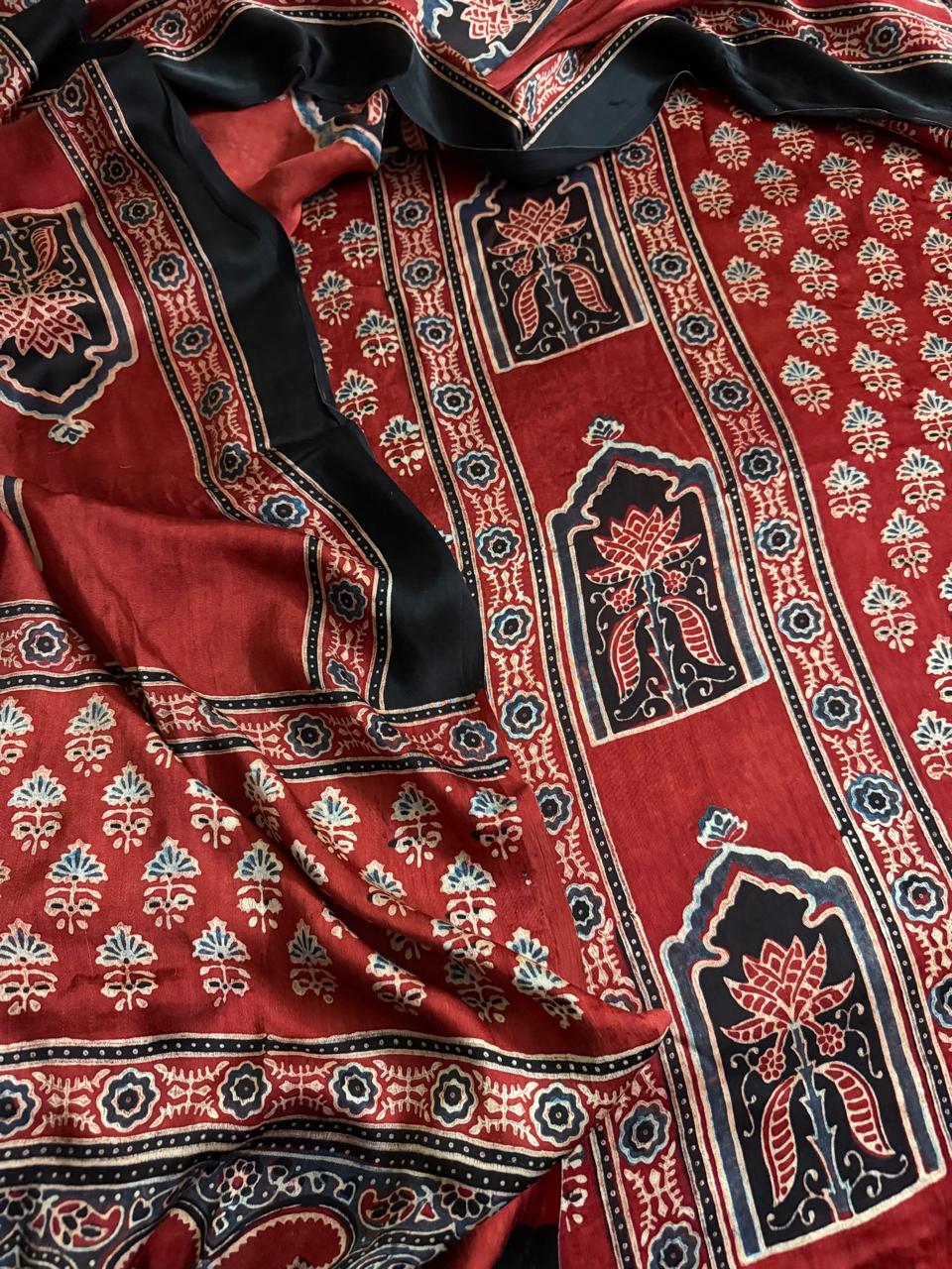 Close-up of red Ajrakh Modal silk kurta fabric with black arch-framed lotus and leaf panel border, scattered red and teal floral sprig body print