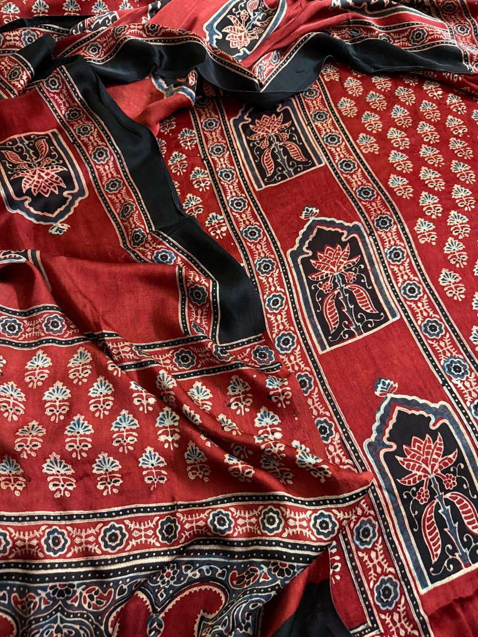 Close-up of red and black Ajrakh Modal silk fabric showing black arch lotus panel border, red teal floral sprig body and intricate dupatta border detail