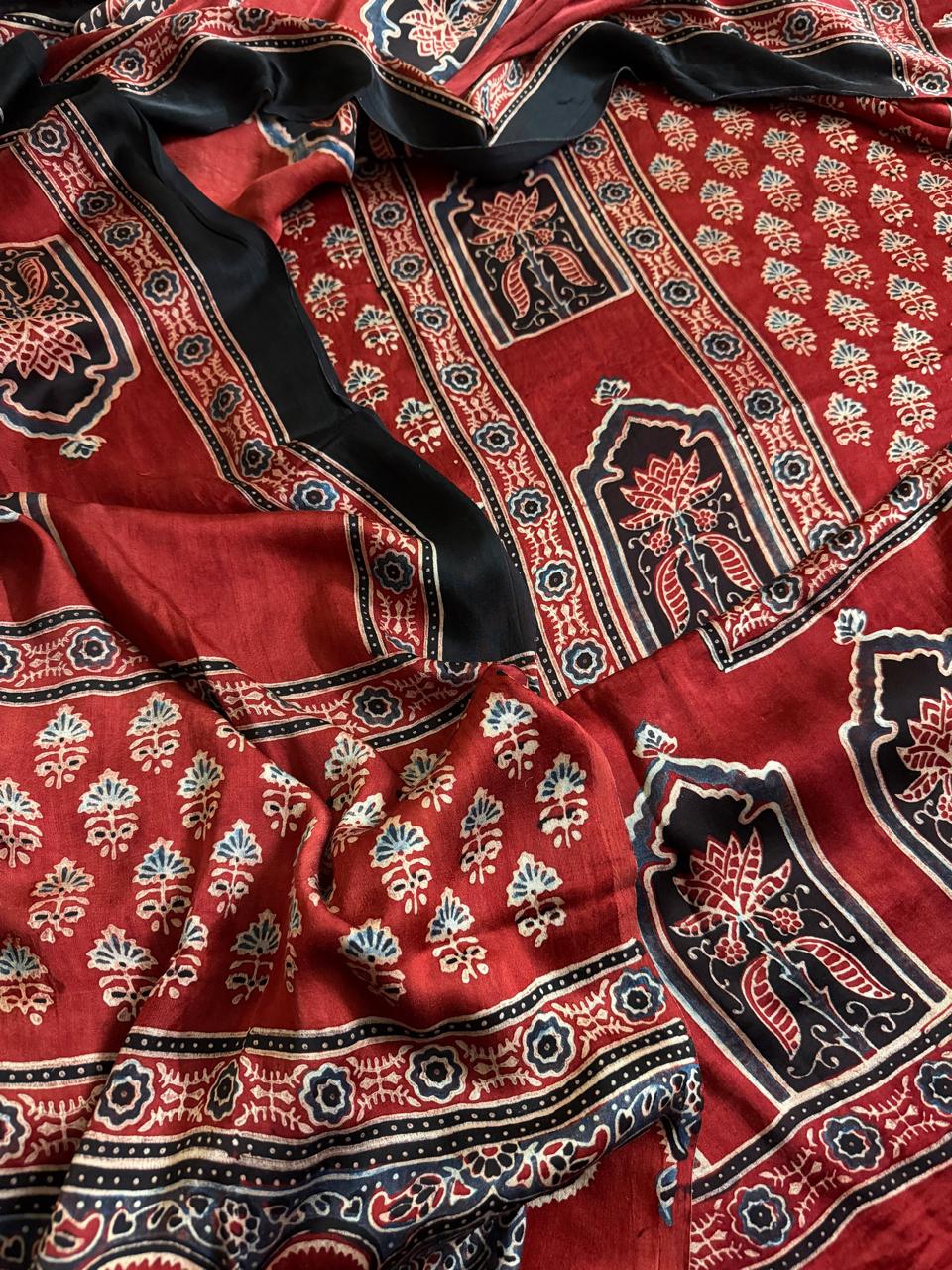 Flat lay of red and black Ajrakh Modal silk kurta dupatta set showing red body with scattered floral sprigs, black arch lotus panel border and intricate dupatta