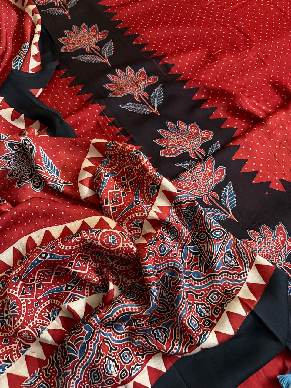 Close-up of red and black Ajrakh Modal silk fabric showing black zigzag border with red lotus florals, red polka dot body and intricate red paisley dupatta