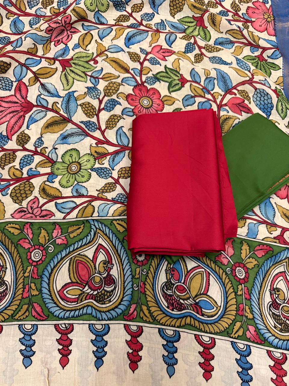 "Flat lay of hand-painted Pen Kalamkari Mangalgiri pattu silk dupatta with folded crimson red and forest green cotton silk suit fabrics – Tantuvana 3-piece set"