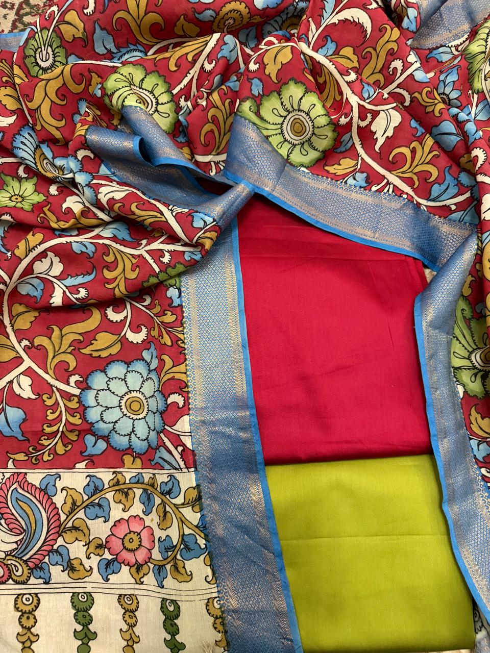 Flat lay of complete 3-piece set – hand pen Kalamkari Mangalgiri silk dupatta with blue Zari border framing crimson red kurta fabric and fresh green cotton silk bottom