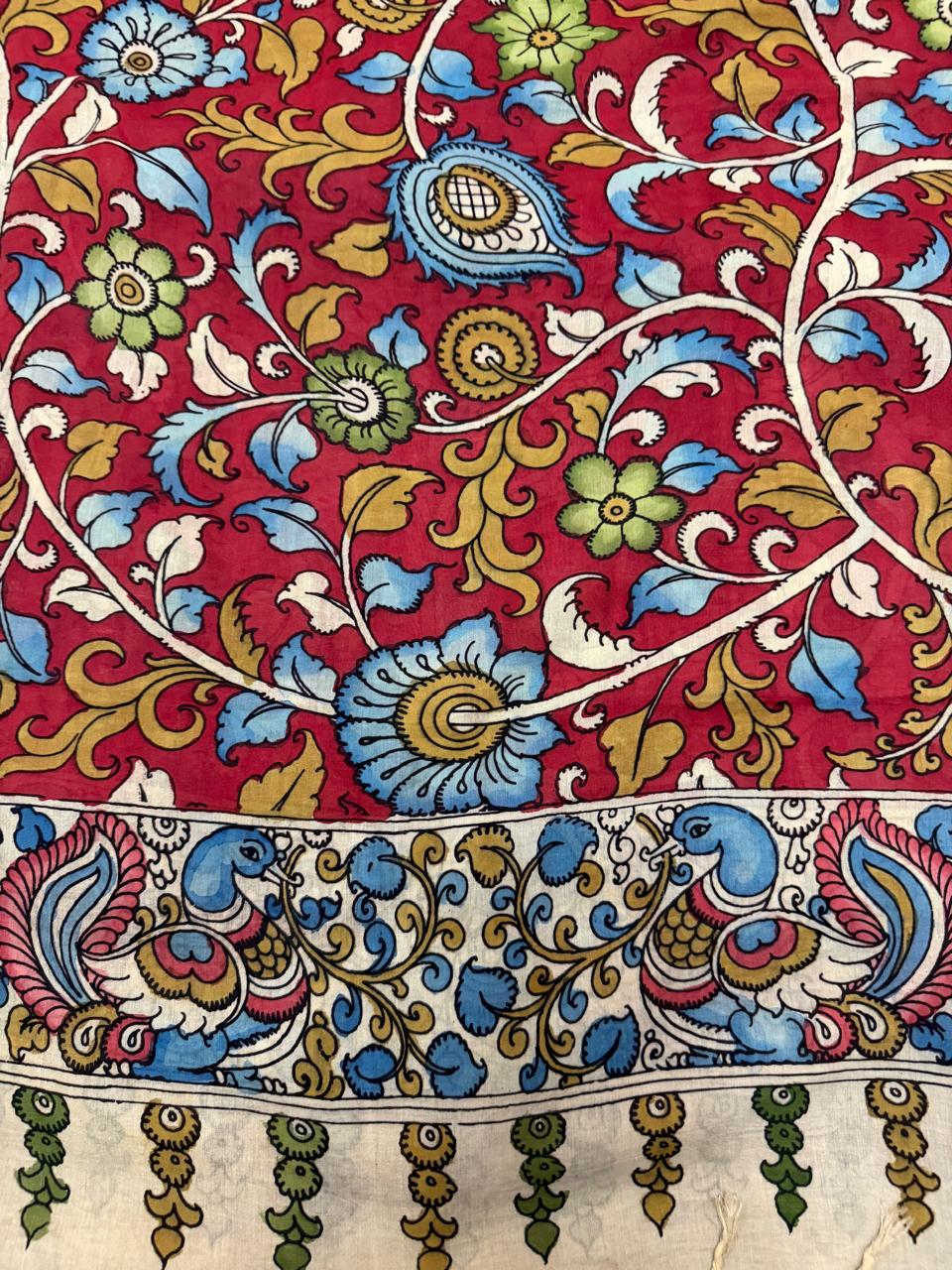 Macro detail of hand pen Kalamkari dupatta body – dense crimson red ground with blue and green floral vine, paisley motifs, and peacock-pair border with tassels