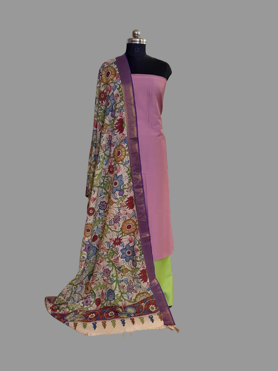 Mannequin display of 3-piece unstitched suit set – rose pink cotton silk kurta with hand pen Kalamkari dupatta draped over shoulder, lime green cotton silk bottom, traditional Indian home setting