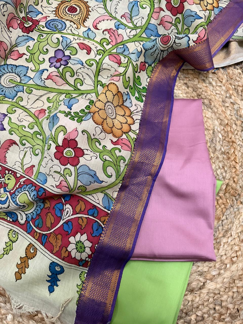 Close-up flat lay of hand pen Kalamkari Mangalgiri silk dupatta body with multicolour floral vine – purple Zari border alongside folded rose pink and lime green cotton silk suit fabrics