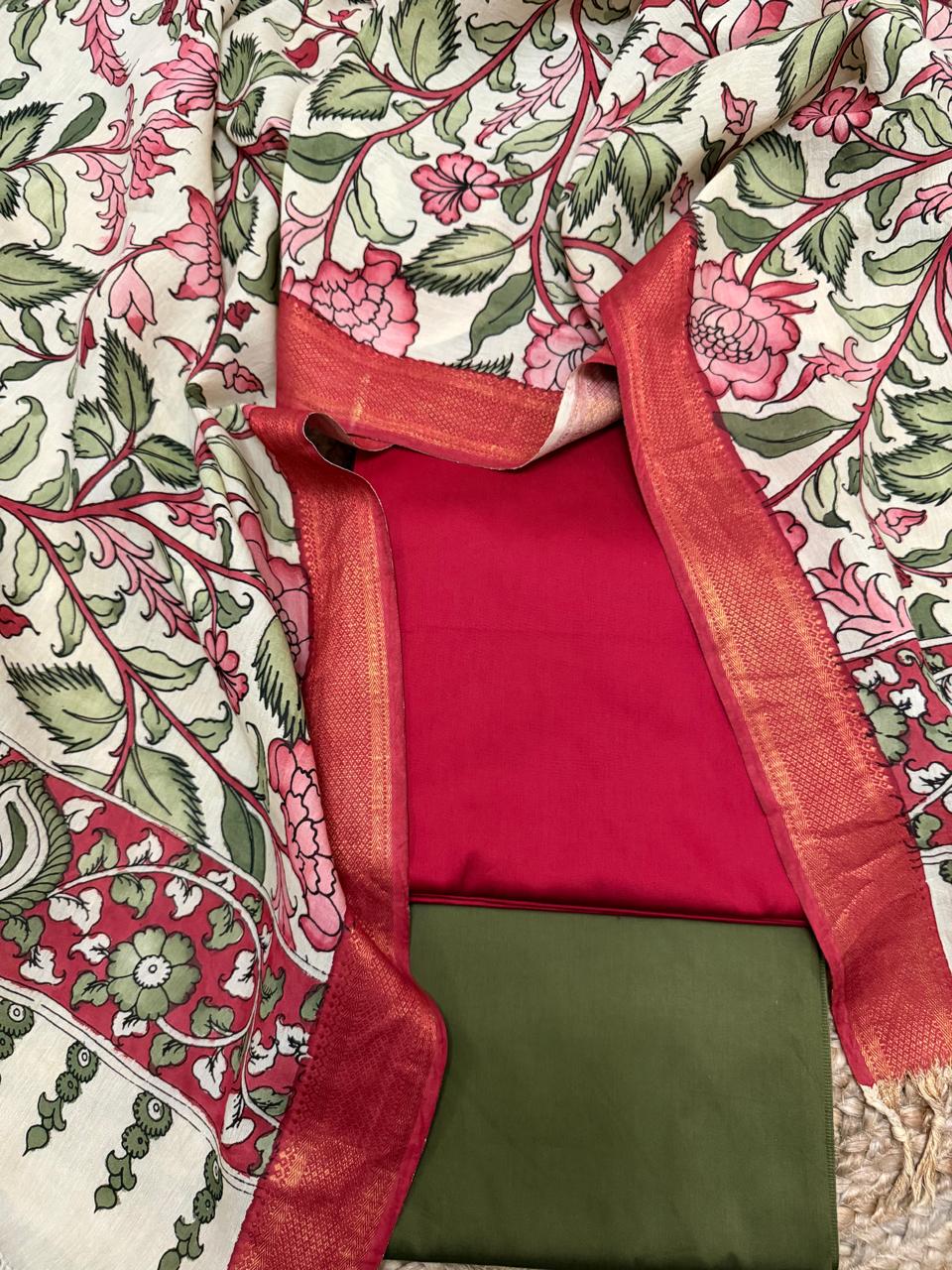 Overhead flat lay showing gold Zari border of hand pen Kalamkari dupatta framing folded red cotton silk kurta and forest green bottom – pink peony floral vine body and crimson peacock border, Mangalgiri silk