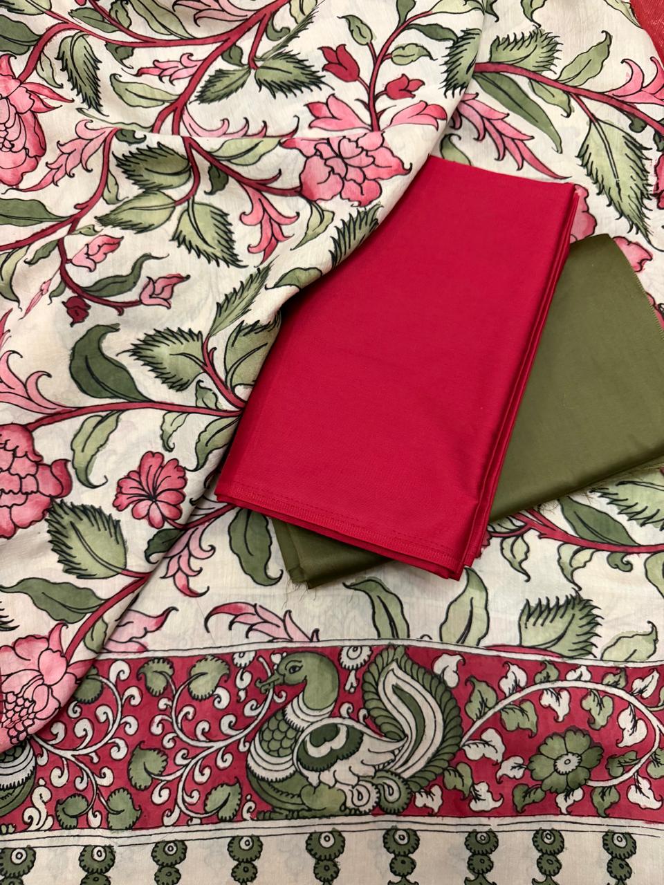 Flat lay of hand pen Kalamkari dupatta over folded red and forest green cotton silk suit fabrics – dense pink floral vine on ivory with peacock-pair border on crimson ground, Mangalgiri silk