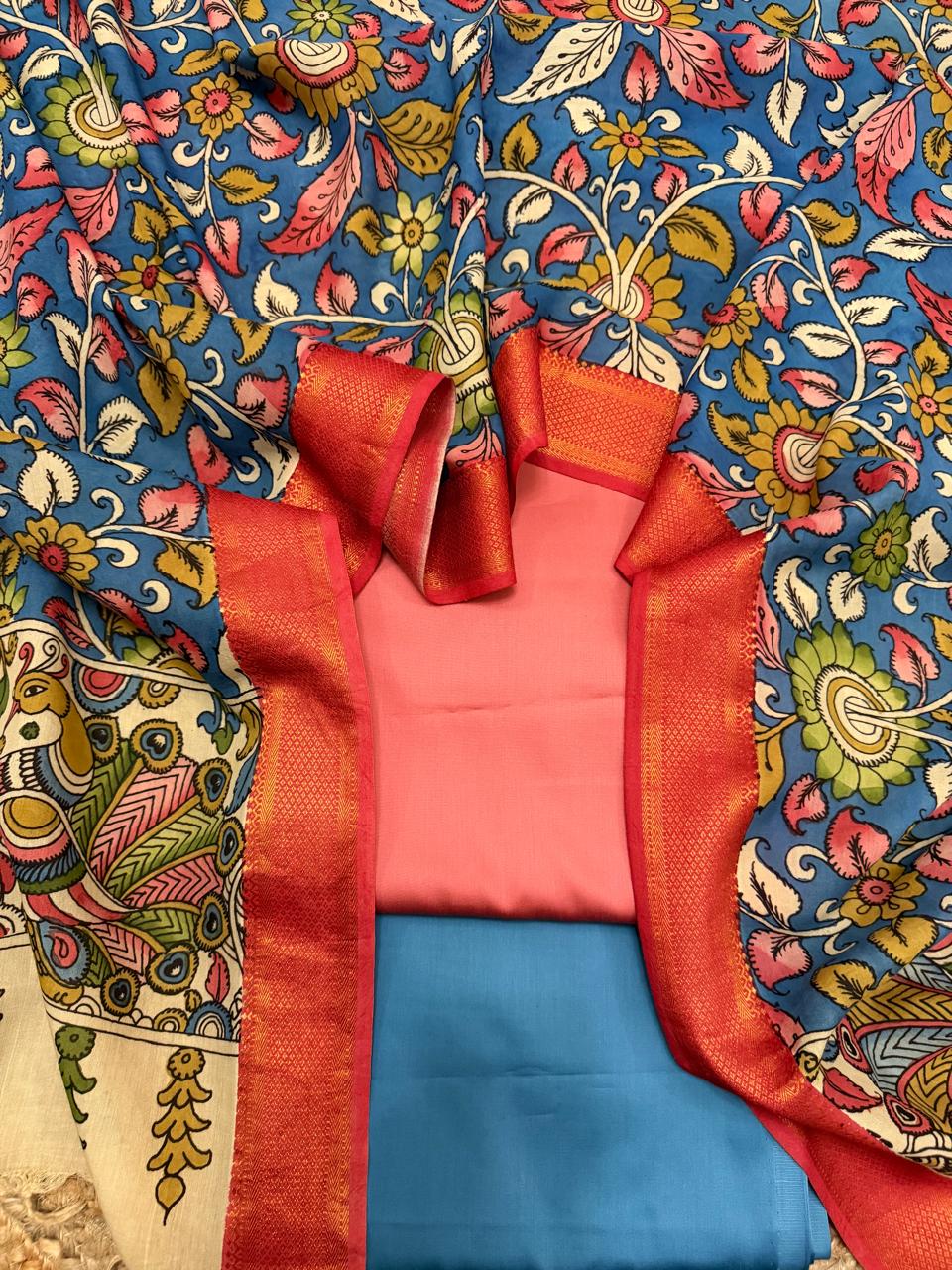 Flat lay showing rose pink cotton silk kurta and slate blue bottom folded inside hand painted Kalamkari dupatta – red-gold Zari border of dupatta framing the suit fabrics, blue dense floral body spread around