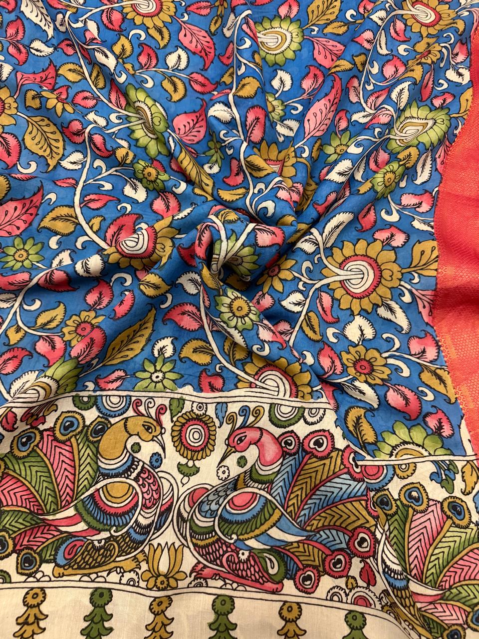 Draped close-up of hand painted Kalamkari dupatta showing blue floral body and ivory peacock-pair pallu – multicolour pink and gold plumage peacocks on ivory ground with red-gold Zari border edge, Mangalgiri silk