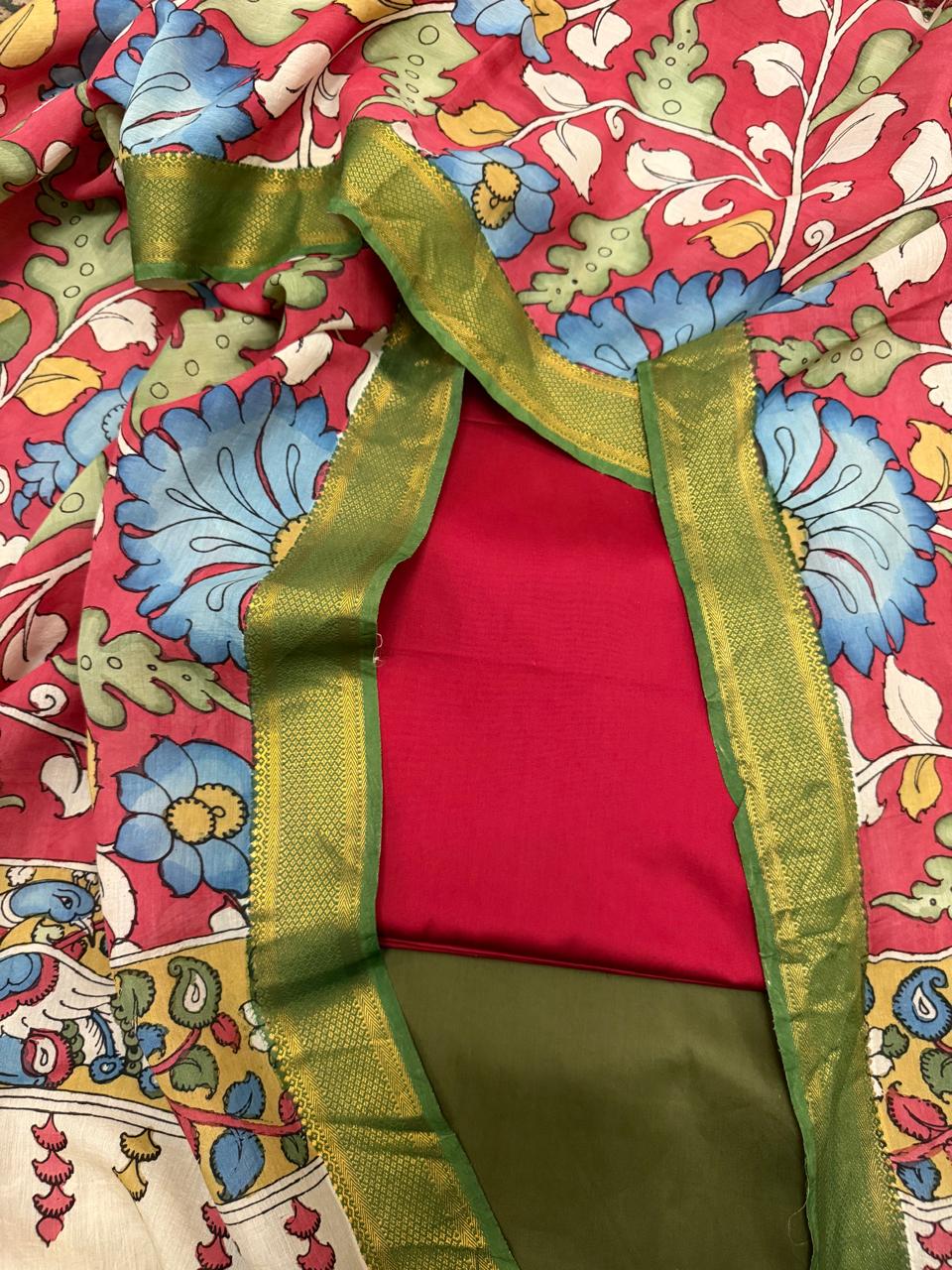 Close-up of green gold Zari dupatta border framing folded red cotton silk kurta and olive forest green bottom – hand pen Kalamkari crimson dupatta with blue floral body spread behind, Tantuvana