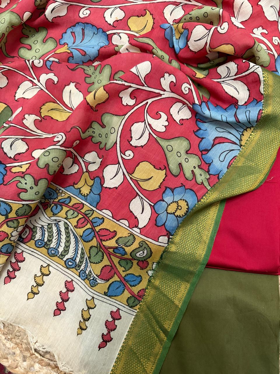 Flat lay of hand pen Kalamkari dupatta over folded red and forest green cotton silk suit fabrics – crimson red ground with blue floral vine and yellow-gold peacock border, Mangalgiri silk