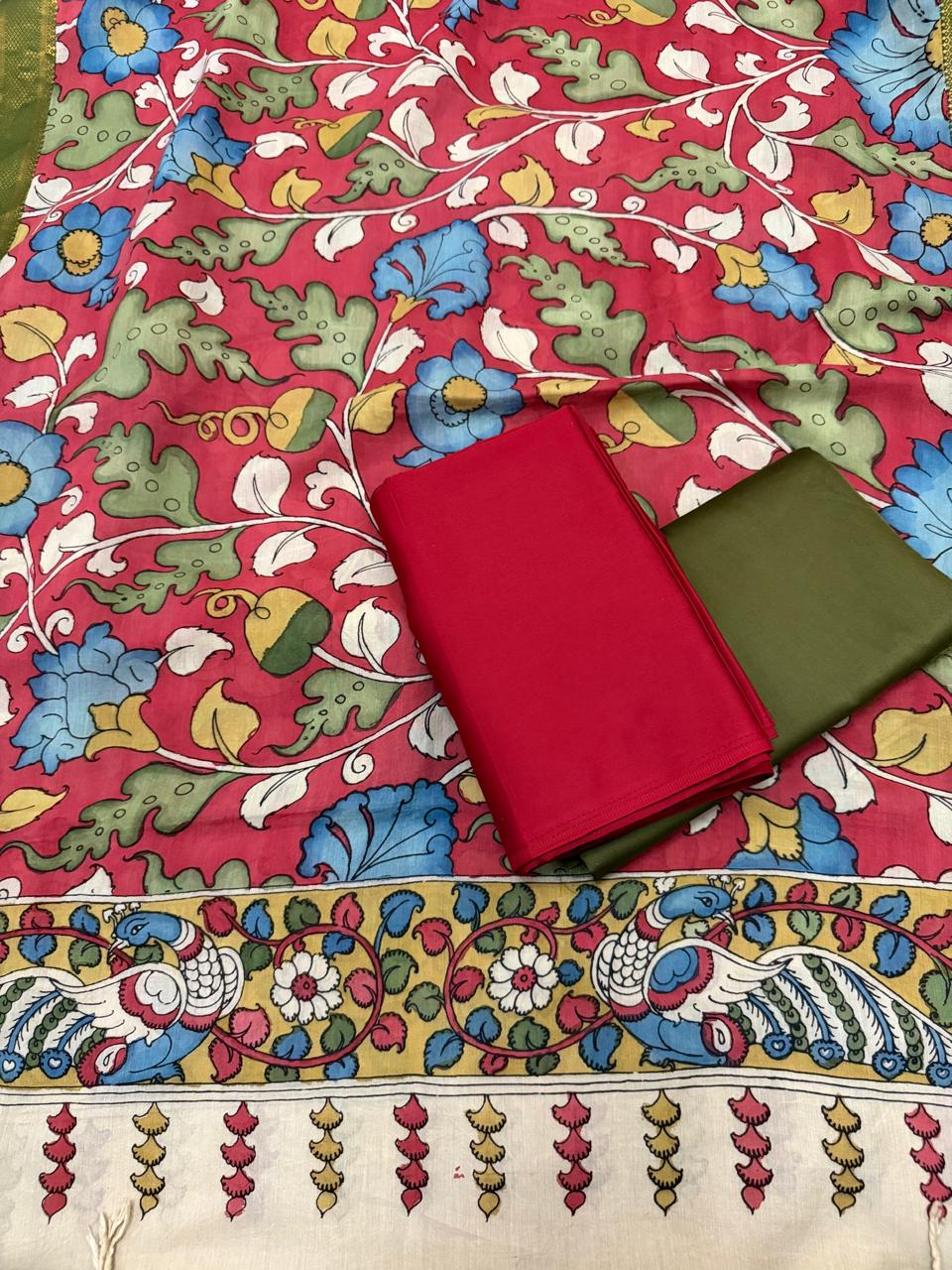 Full spread flat lay of hand pen Kalamkari dupatta body with folded red kurta and forest green bottom – crimson red ground dense blue floral vine with yellow-gold peacock pallu border and tassel fringe