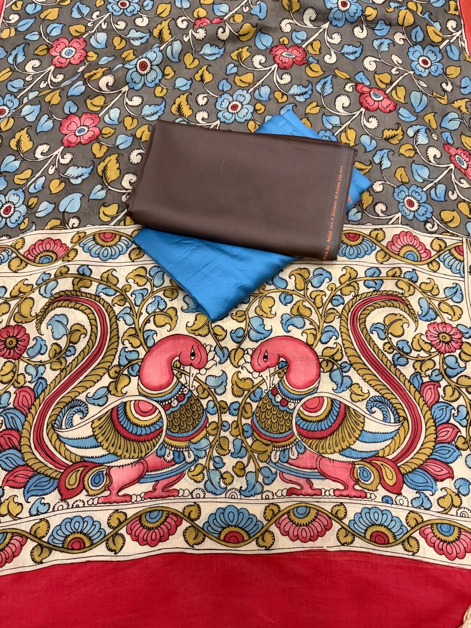 Overhead flat lay of hand painted Kalamkari dupatta pallu showing facing peacock-pair motif on ivory ground with blue and gold foliage, grey floral body above, folded state blue and charcoal brown cotton silk