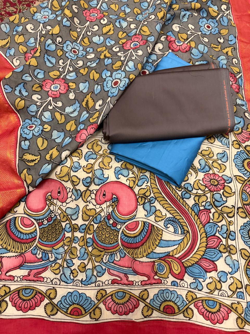 Full spread flat lay of hand painted Kalamkari dupatta – grey ground dense pink and blue floral vine body, ivory peacock-pair pallu with red-orange Zari border, state blue and charcoal brown suit fabrics