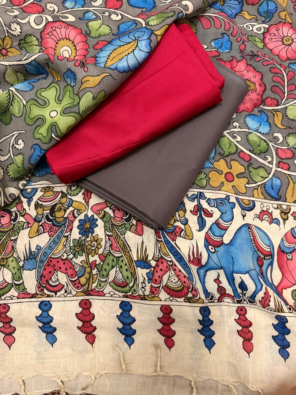 Flat lay of hand painted Kalamkari dupatta body over red and charcoal brown suit fabrics – grey ground dense pink lotus and blue floral vine with white scroll, ivory mythological pallu