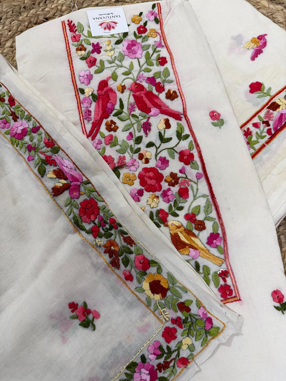 Overhead flatlay of cream cotton Parsi Gara hand-embroidered 3-piece unstitched suit set – bird and floral jaal neckline panel, scattered bird butti on kurta, floral border dupatta and plain bottom fabric