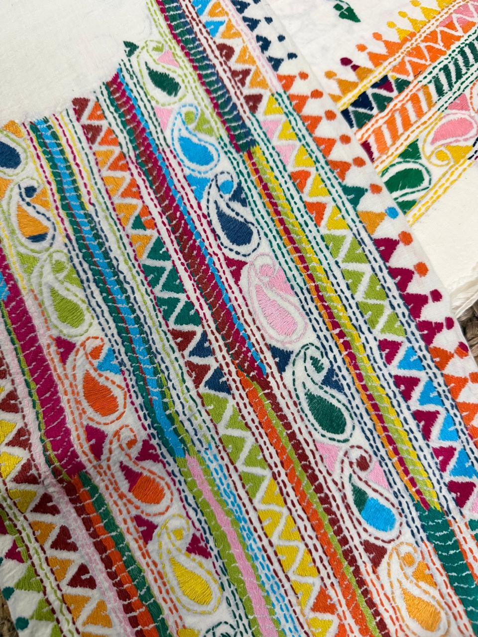Macro detail of Kantha hand embroidery on white cotton kurta – dense multicolour horizontal stripes with paisley and geometric triangle motifs in red, blue, green, yellow and orange threads