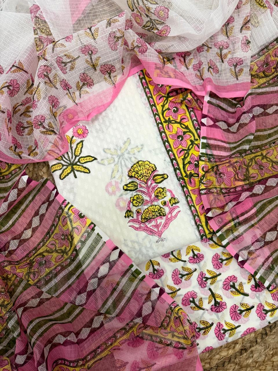 Overhead flatlay of white cotton Mughal block print unstitched kurta – pink and yellow marigold floral butti placement with yellow floral vine border strip, pink floral Kota Doria dupatta and pink floral bottom fabric draped