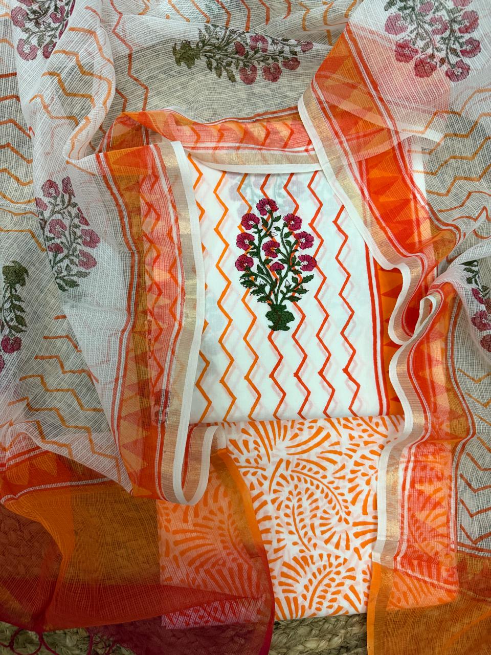 Straight overhead flatlay of white cotton Mughal block print unstitched suit set – orange zigzag chevron kurta with pink floral butti placement, orange paisley bottom fabric and sheer Kota Doria dupatta with orange chevron and border